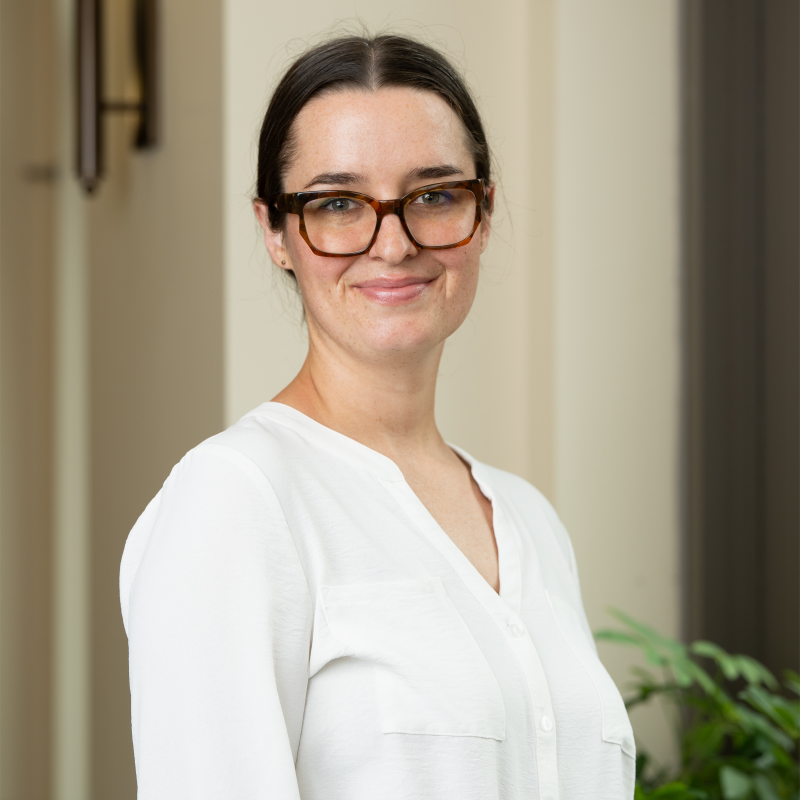 Professional headshot of woman with light skin, brown hair, and glasses.