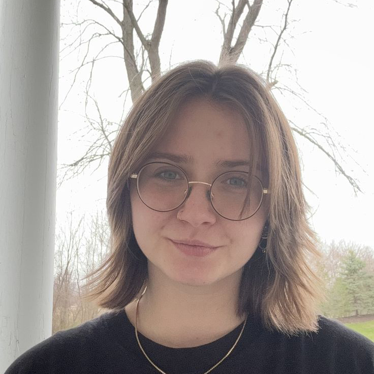 Emma smiling, brown hair, glasses, black t-shirt